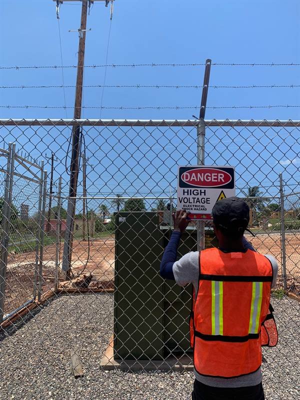 Worker installing high voltage danger signage at a substation fence for the NIC EVAD water project